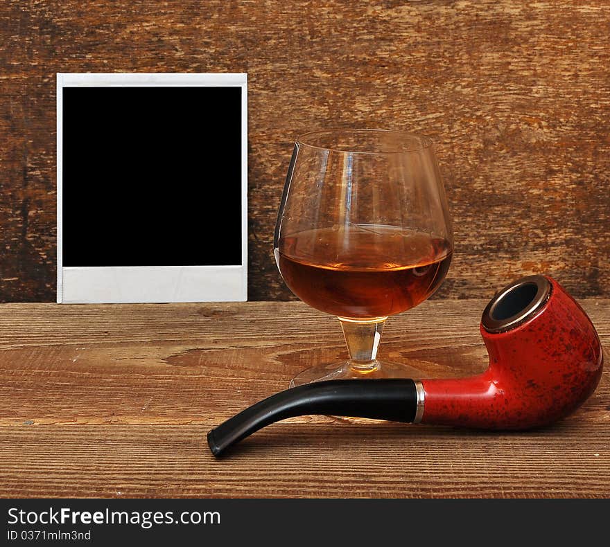 Old photo, pipe and glass of cognac on wood background