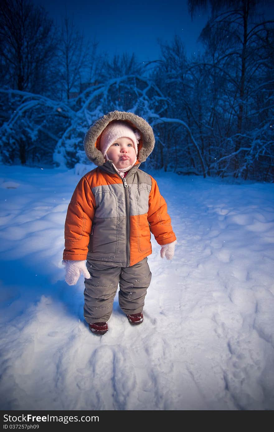 Adorable baby walking in evening park. Stay on snow road look up