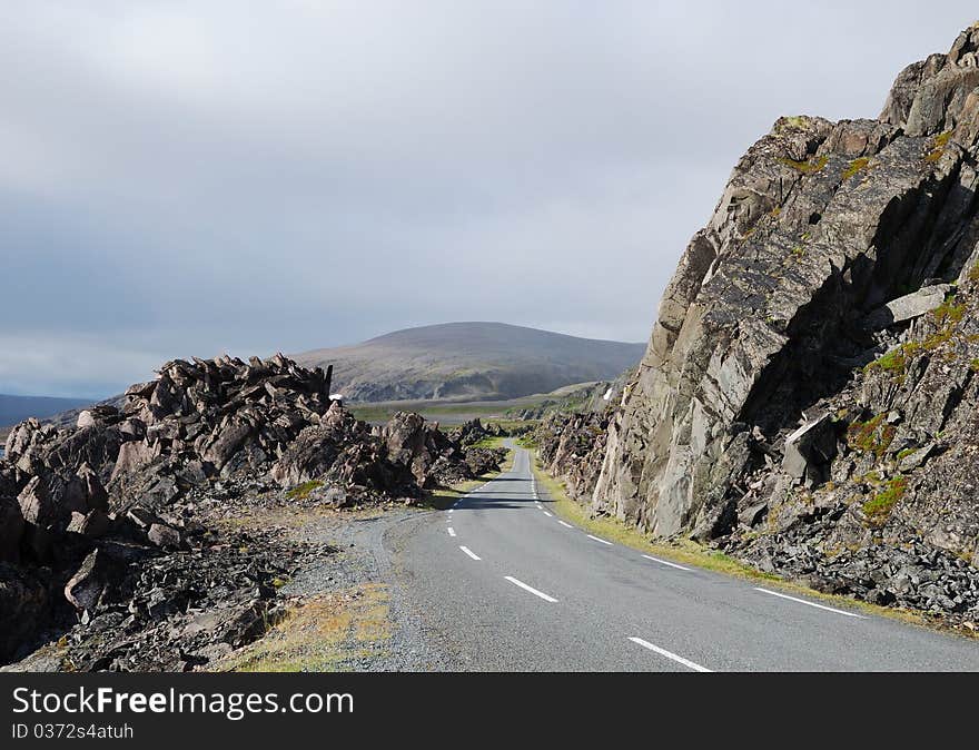 Asphalt road is meandering between among rocks of north Norwegian coast. This is the road to Hamningberg. Highway is photographed with diminishing perspective. Asphalt road is meandering between among rocks of north Norwegian coast. This is the road to Hamningberg. Highway is photographed with diminishing perspective.