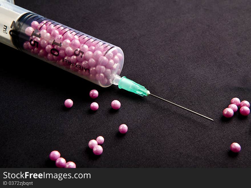 Syringe filled with pink candy on a black background