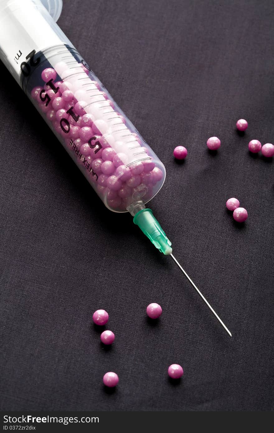 Syringe filled with pink candy on a black background