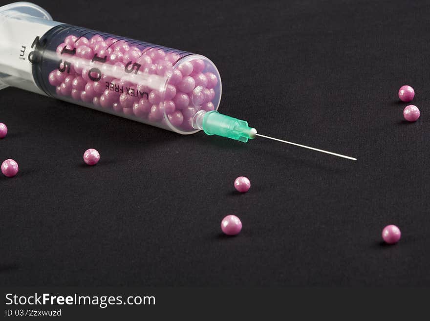 Syringe filled with pink candy on a black background