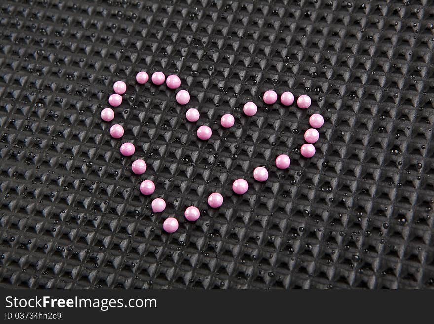 Heart shape made with candy on rubber black background