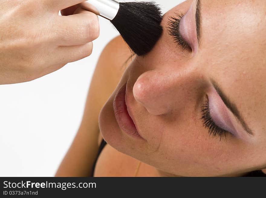 Close up of the face of a young model with a makeup artist applying blush with a concealer foundation brush. Close up of the face of a young model with a makeup artist applying blush with a concealer foundation brush