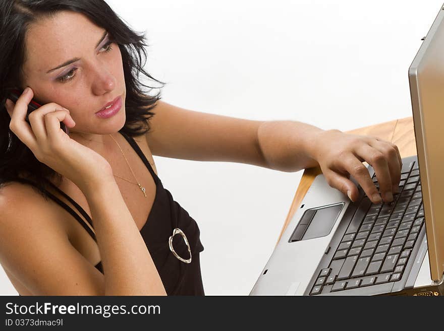 Young smiling brunette business woman typing on a laptop and talking on a cellphone. Young smiling brunette business woman typing on a laptop and talking on a cellphone