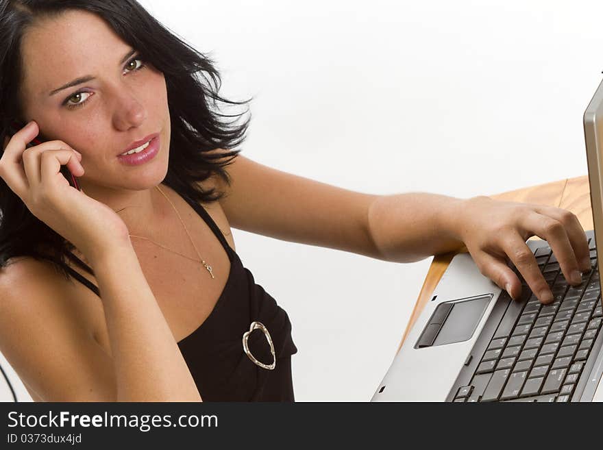 Young smiling brunette business woman typing on a laptop and talking on a cellphone. Young smiling brunette business woman typing on a laptop and talking on a cellphone