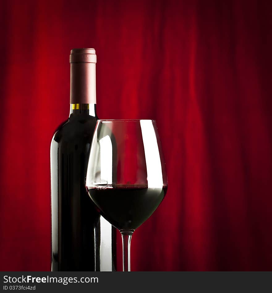 A glass of red wine and a bottle on red background