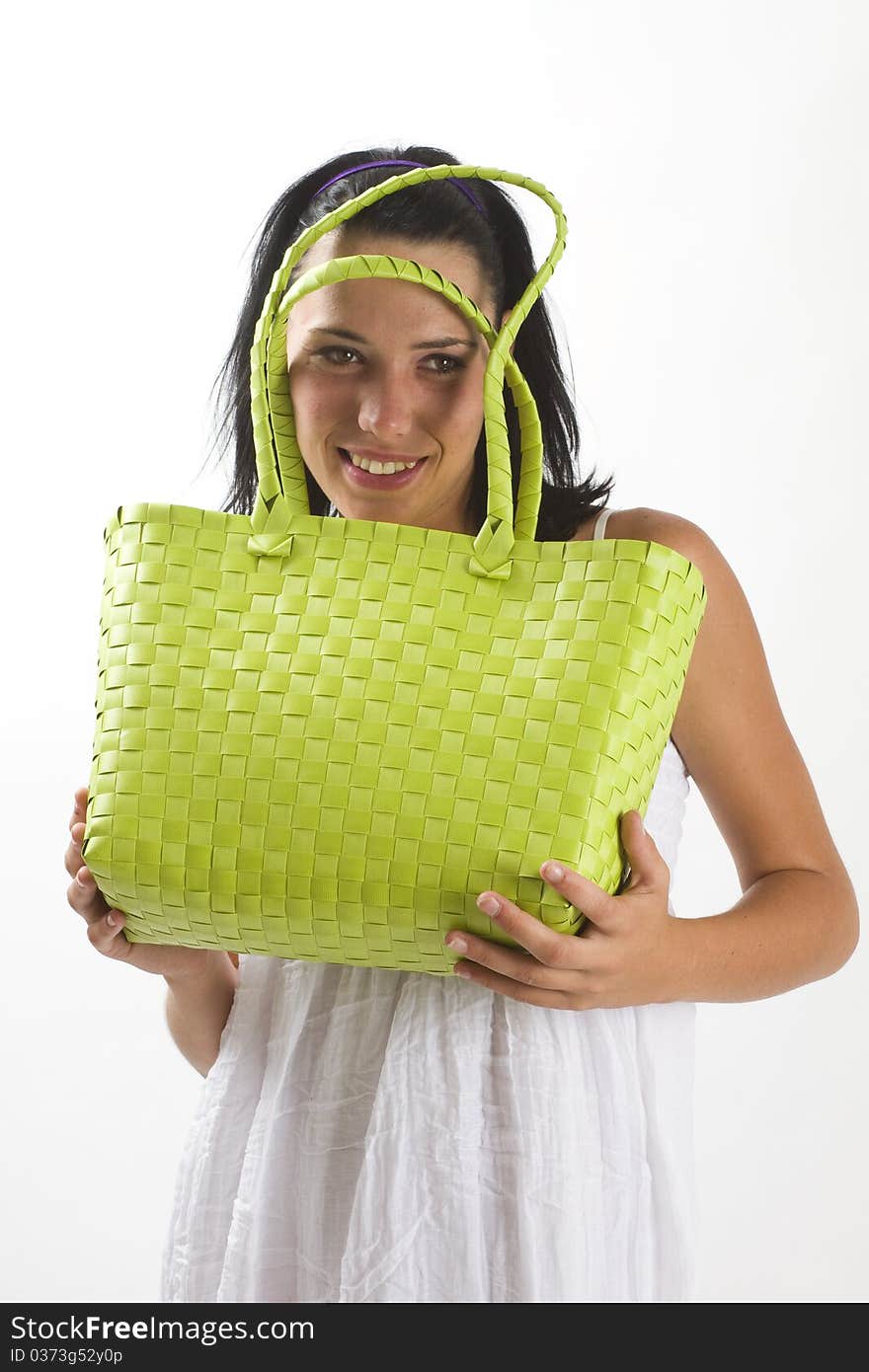 Young tanned healthy woman in a white summer cotton dress holding a green woven shopping bag. Young tanned healthy woman in a white summer cotton dress holding a green woven shopping bag