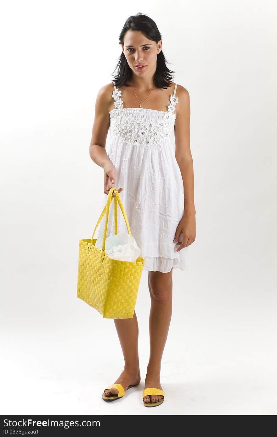 Young tanned healthy woman in a white summer cotton dress and yellow sandals carrying a yellow woven shopping bag. Young tanned healthy woman in a white summer cotton dress and yellow sandals carrying a yellow woven shopping bag