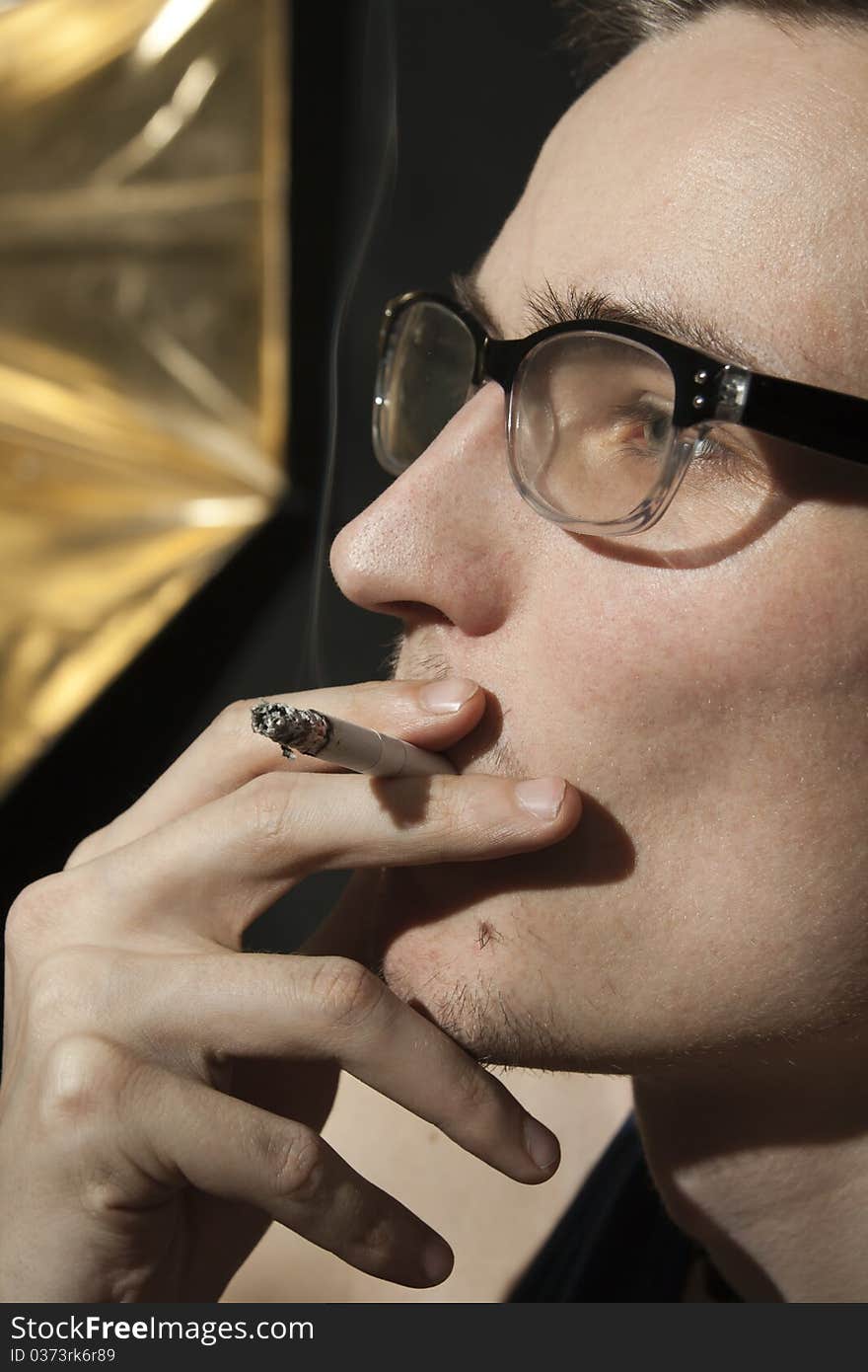 Pensive young man in glasses smoking a cigarette. Pensive young man in glasses smoking a cigarette