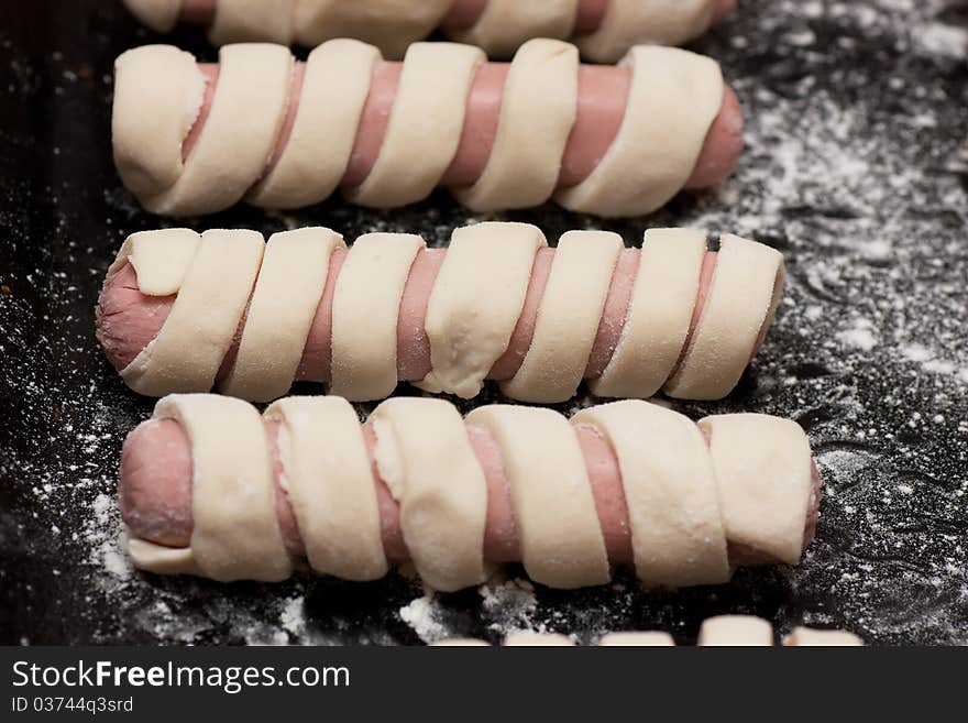 Raw sausage rolls in pastry on a baking tray