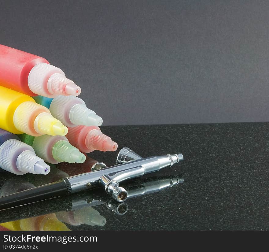 A pyramid of colourful paints and a silver airbrush on a dark background. A pyramid of colourful paints and a silver airbrush on a dark background