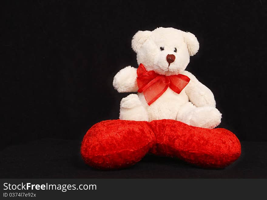 White teddy bear sitting on a heart shaped pillow isolated on black background