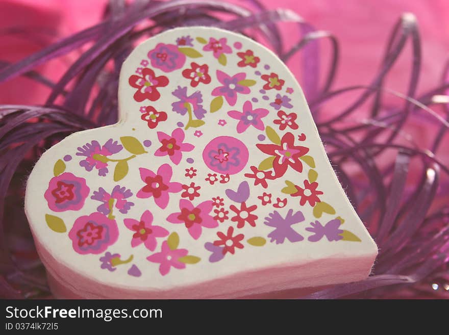 Heart shaped box with flower pattern on a bed of purple rafflia with pink background.