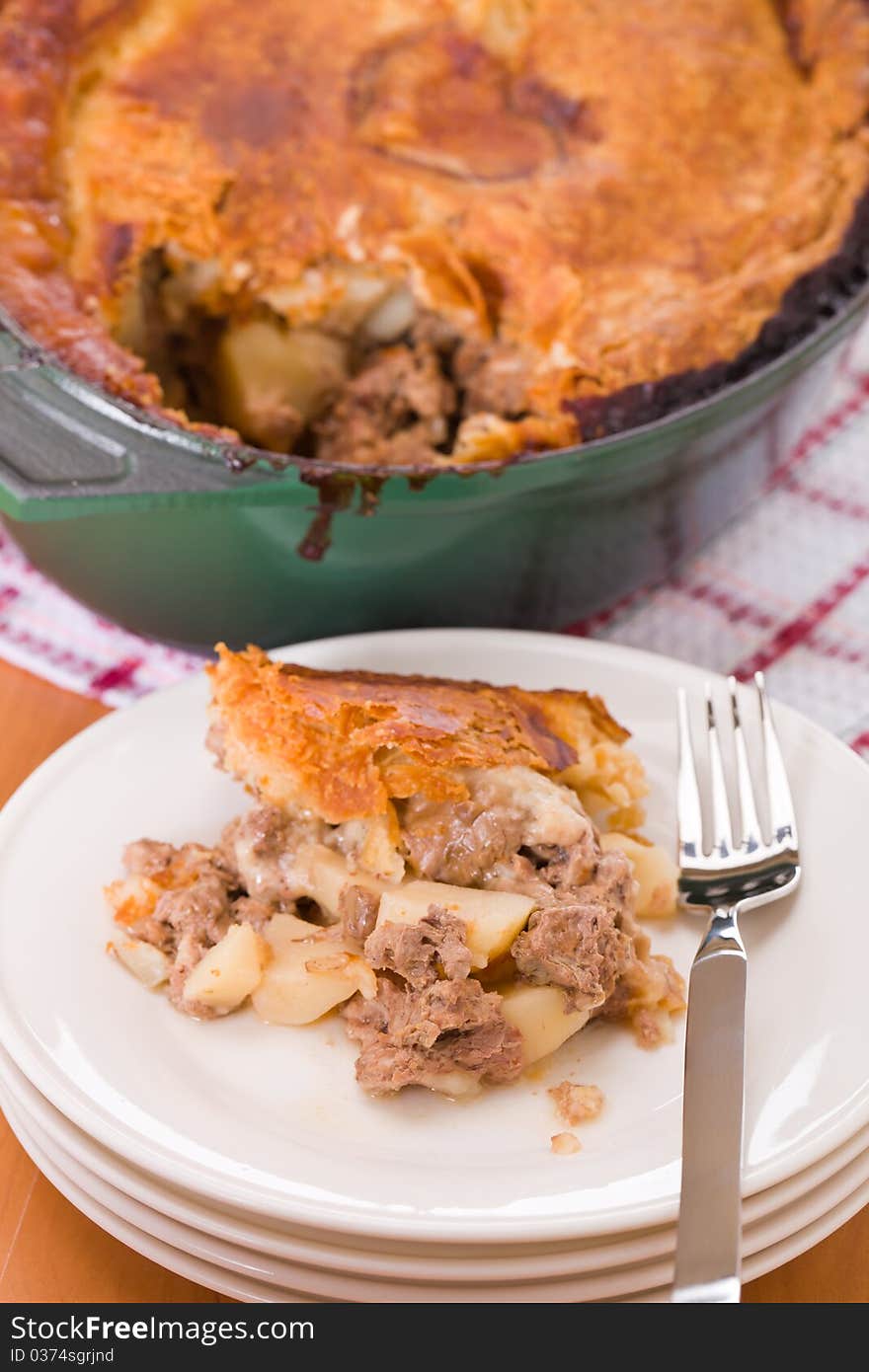 Pot pie with beef, veal and pork meat in a green oven cookware. Portion in a white plate.Very shallow depth of field. Pot pie with beef, veal and pork meat in a green oven cookware. Portion in a white plate.Very shallow depth of field.