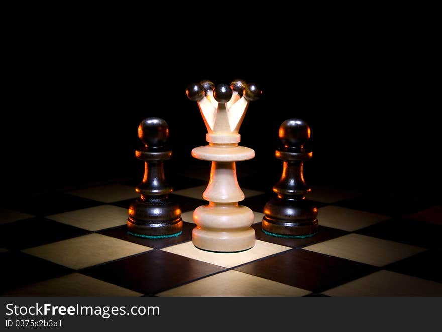 Queen and two pawns on a chess board. A dark art background. Queen and two pawns on a chess board. A dark art background.