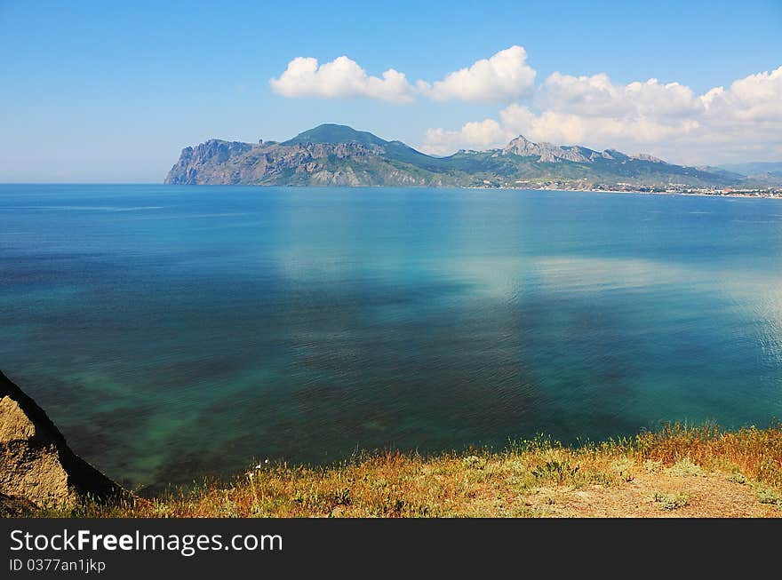 Seascape - a beautiful reflection on the water. On the horizon - an ancient volcano. Grass and flower. Seascape - a beautiful reflection on the water. On the horizon - an ancient volcano. Grass and flower