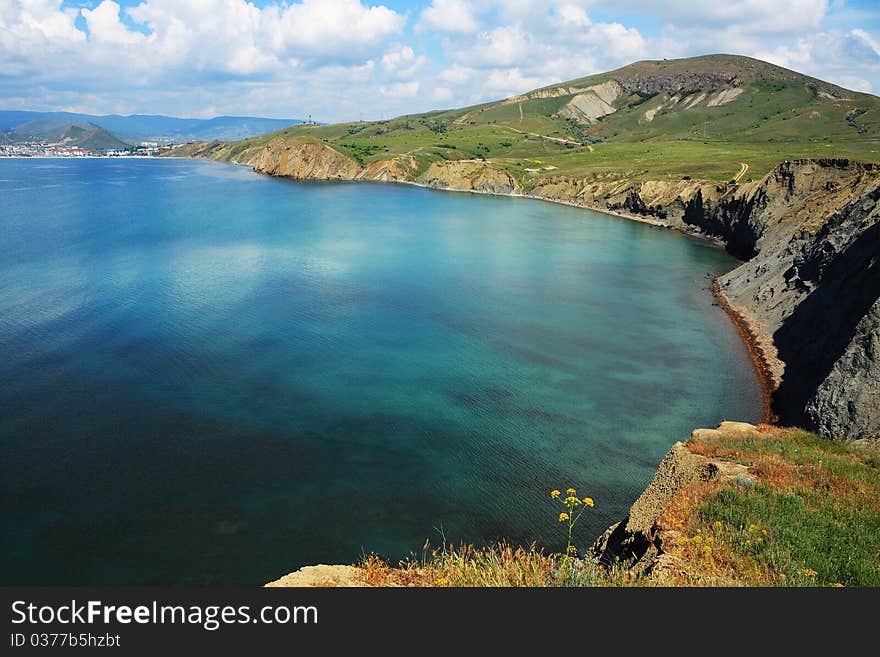 Seascape - a beautiful reflection on the water. Contrast color turquoise sea water and clay of coast. Green grass and flower. Seascape - a beautiful reflection on the water. Contrast color turquoise sea water and clay of coast. Green grass and flower