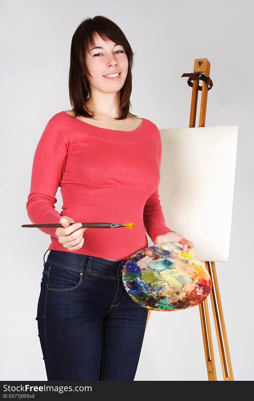 Young girl in red shirt standing near easel, holding brush and palette, smiling. Young girl in red shirt standing near easel, holding brush and palette, smiling