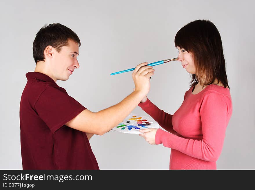 Man touching nose of young girl by brush, holding palette, side view