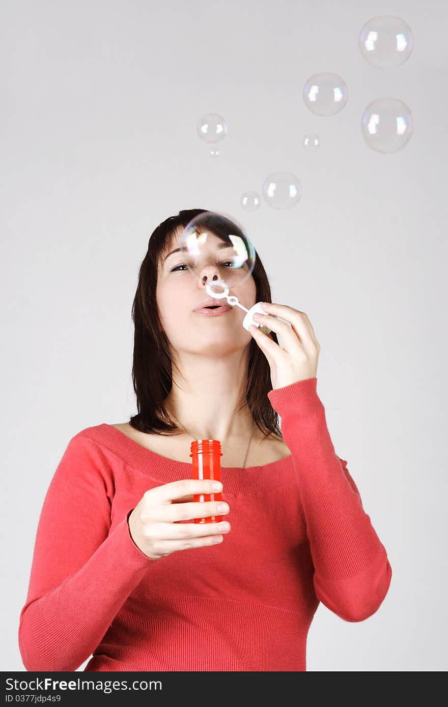 Young brunette woman in red shirt blowing out soap bubbles, vertical