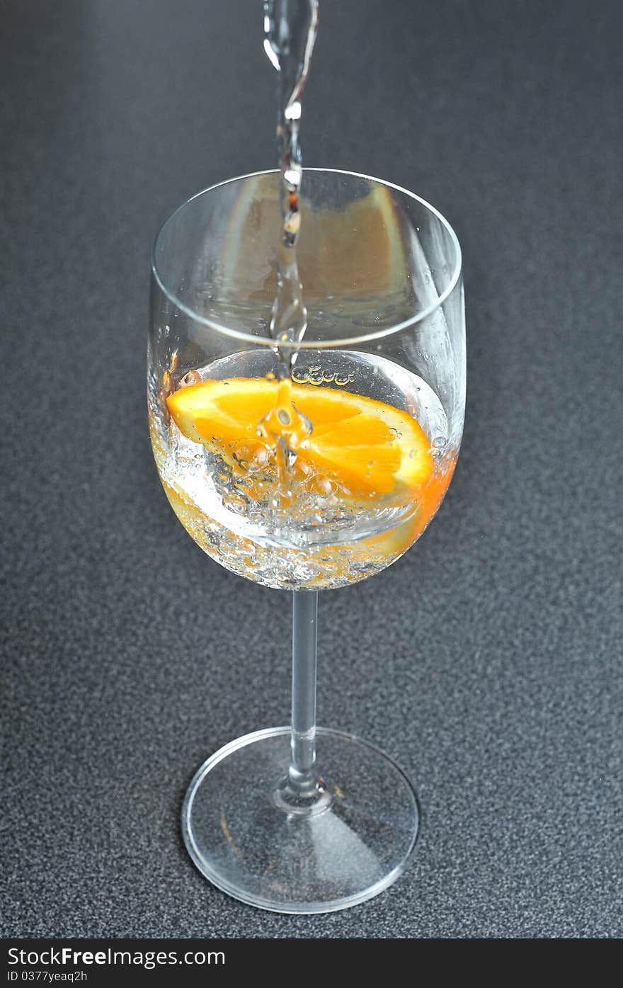 Pouring water into glass with orange