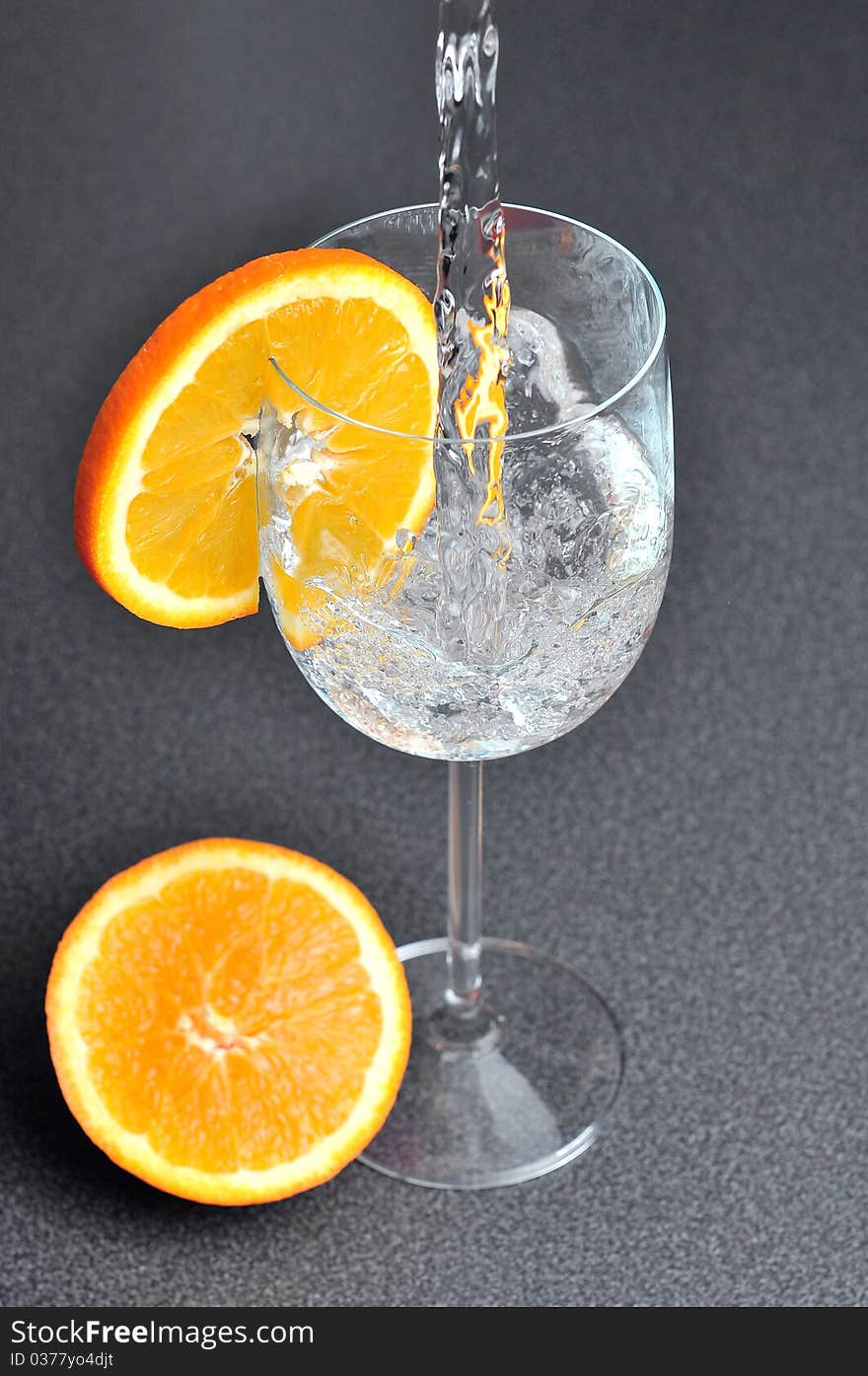 Pouring water into glass with orange