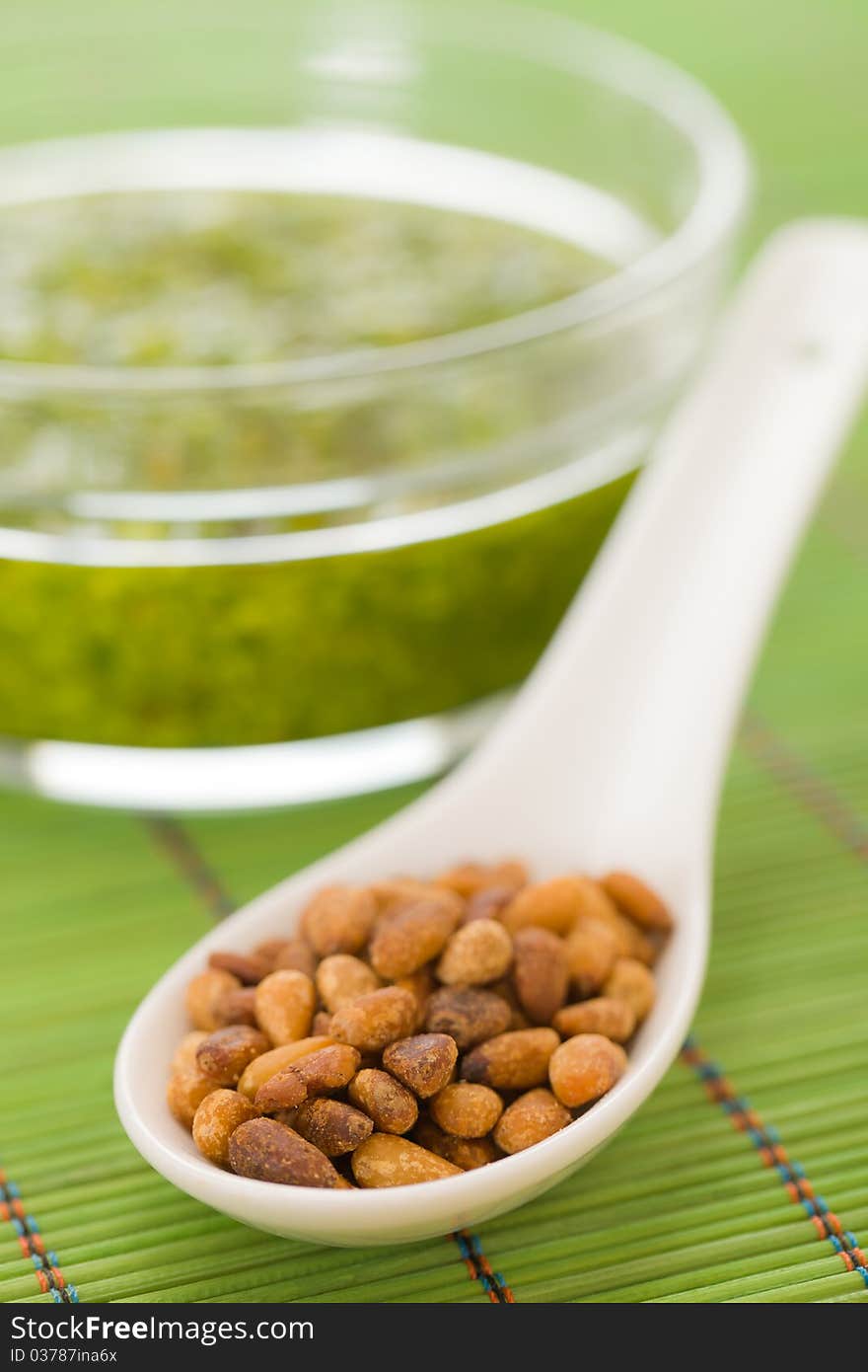 Pine nuts in a spoon with pesto sauce in the background. Extreme shallow depth of field.