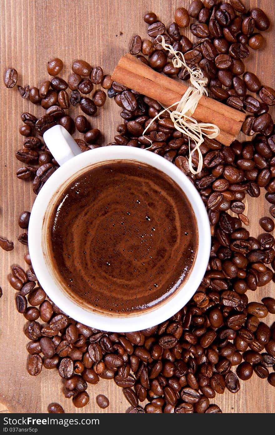 Cup of black coffee and fragrant fried coffee beans and cinnamon on a wooden table. Cup of black coffee and fragrant fried coffee beans and cinnamon on a wooden table