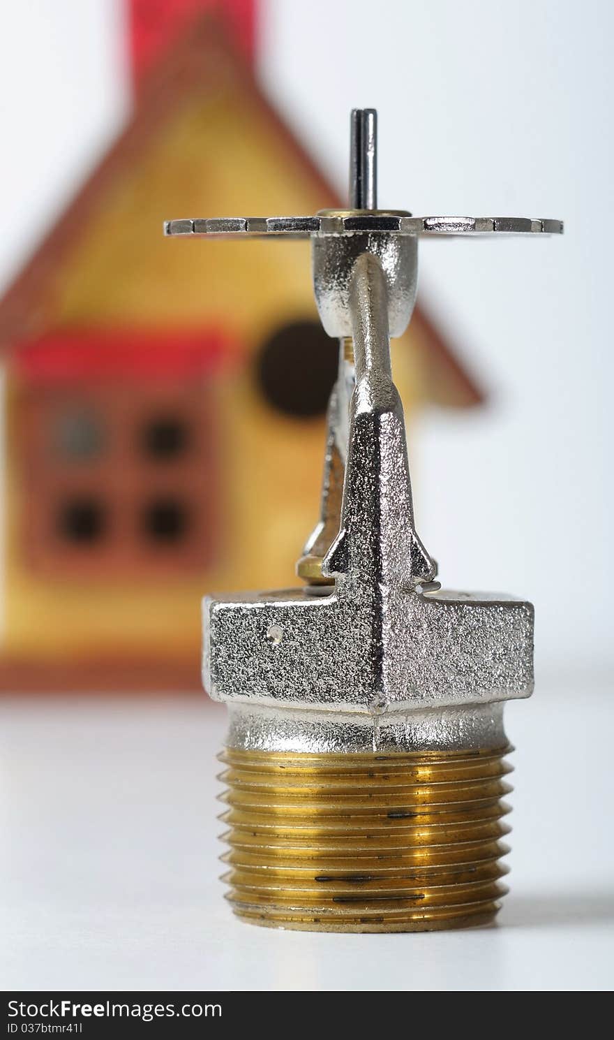 Close up image of fire sprinkler on white. Fire sprinklers are part of an integrated water piping system designed for life and fire safety. Replica of house added to background. Close up image of fire sprinkler on white. Fire sprinklers are part of an integrated water piping system designed for life and fire safety. Replica of house added to background.