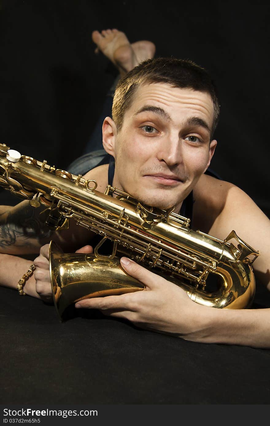 Young jazzman lie on the floor with saxophone