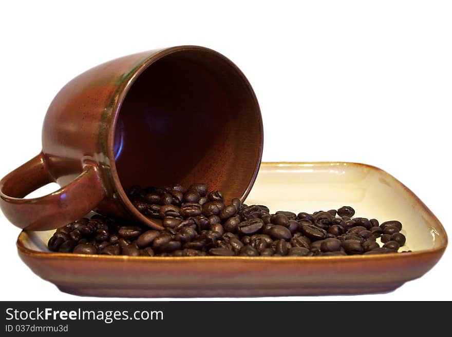 Coffee beans spilling into dish from cup - isolated against white. Coffee beans spilling into dish from cup - isolated against white