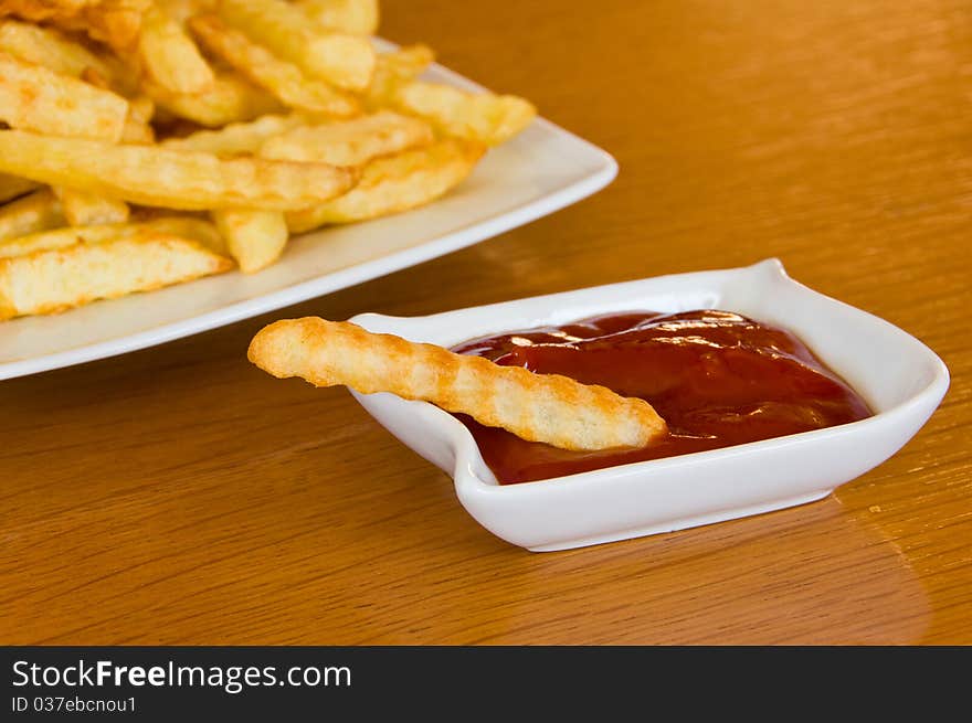 Close-up of a single french fry in bowl of ketchup, plate with fries in the background. Close-up of a single french fry in bowl of ketchup, plate with fries in the background