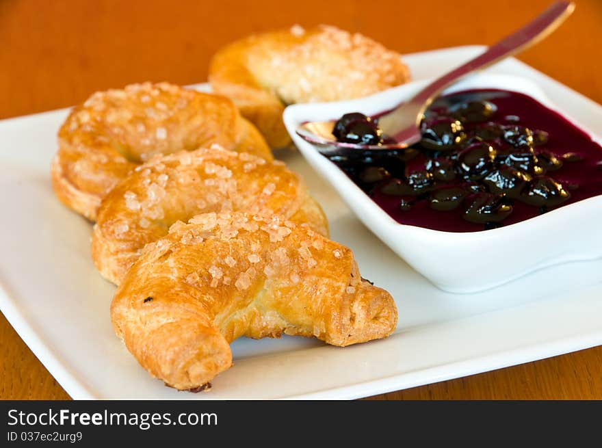 White plate of freshly baked, golden croissants with a bowl of blackberry jelly and a spoon. White plate of freshly baked, golden croissants with a bowl of blackberry jelly and a spoon