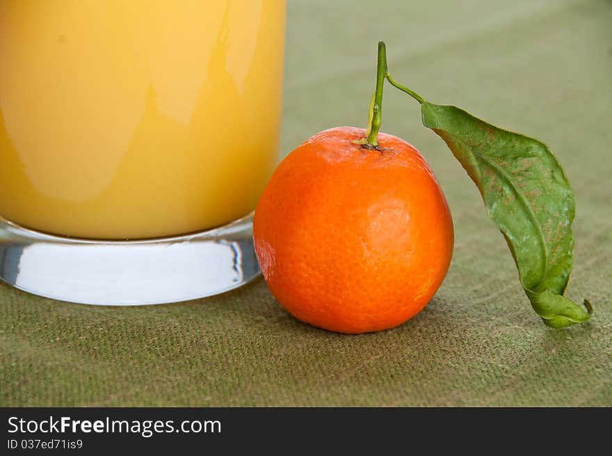 Close-up of a single orange fruit with a glass of orange juice on green napkin. Close-up of a single orange fruit with a glass of orange juice on green napkin