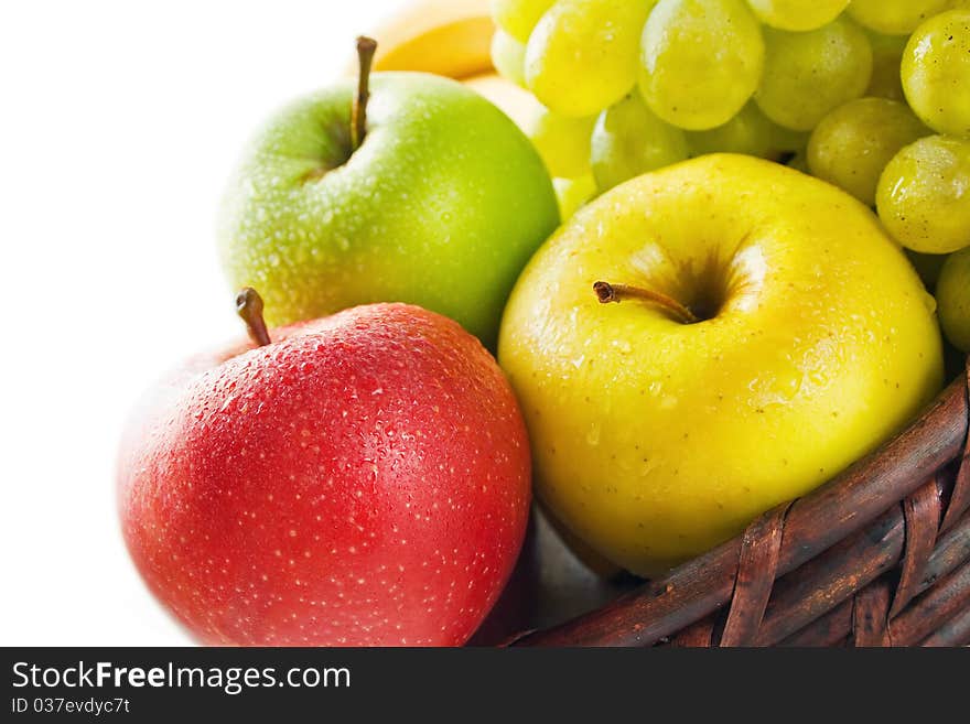 Three apples in different colors placed in a wicker basket with some grape and banana isolated on white. Three apples in different colors placed in a wicker basket with some grape and banana isolated on white