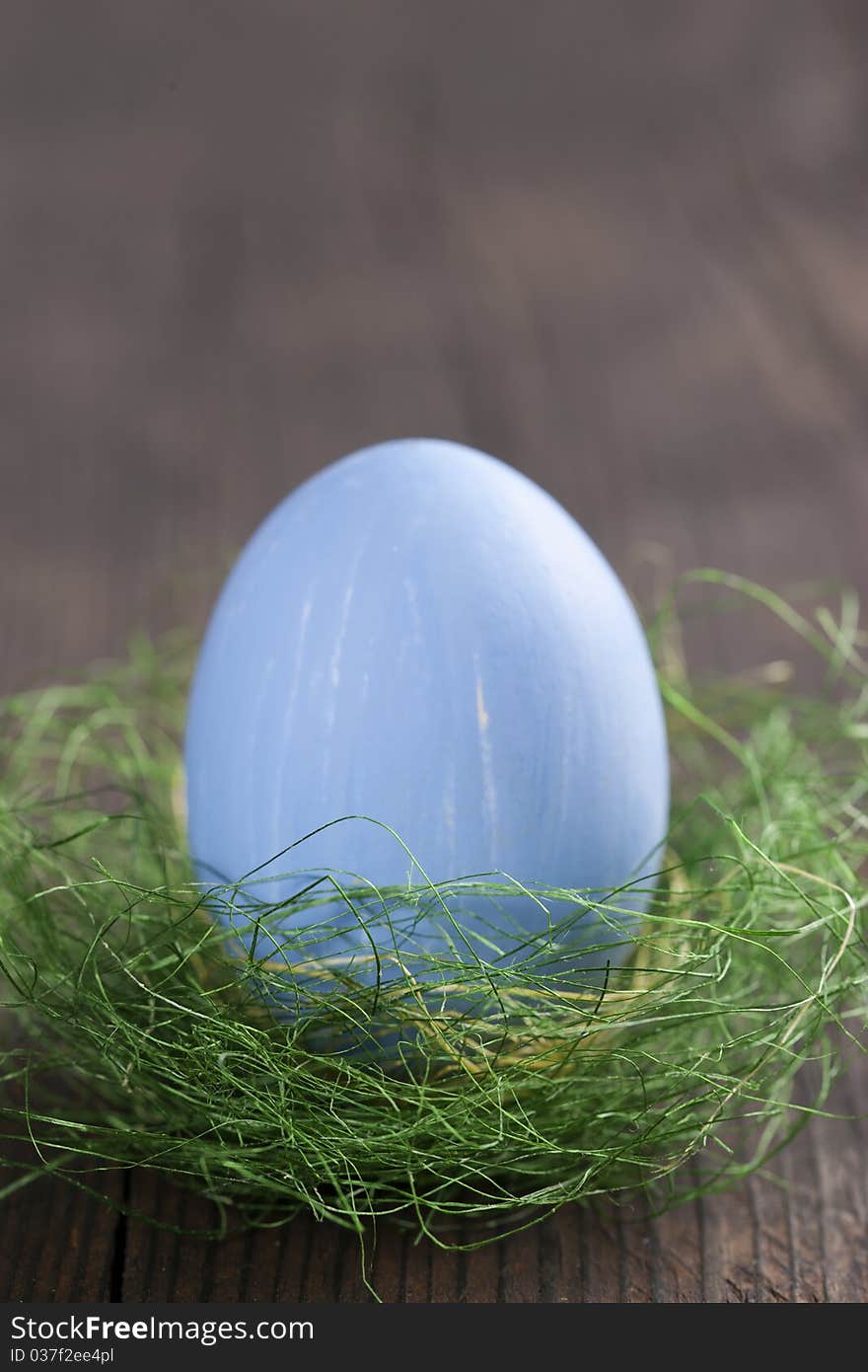 Blue easter egg in nest on wooden background