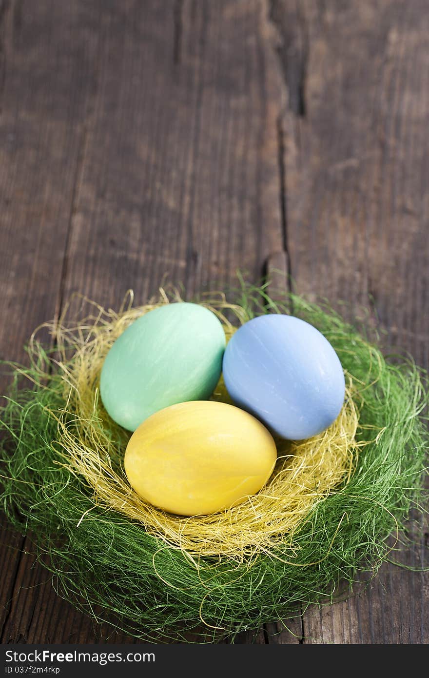 Colorful easter eggs in nest on wooden background