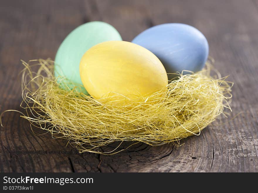 Colorful easter eggs in nest on wooden background