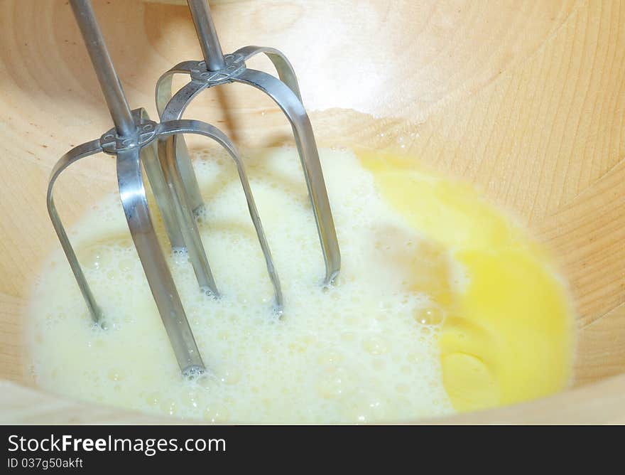 Beating eggs with an electric mixer in a wooden bowl. Beating eggs with an electric mixer in a wooden bowl