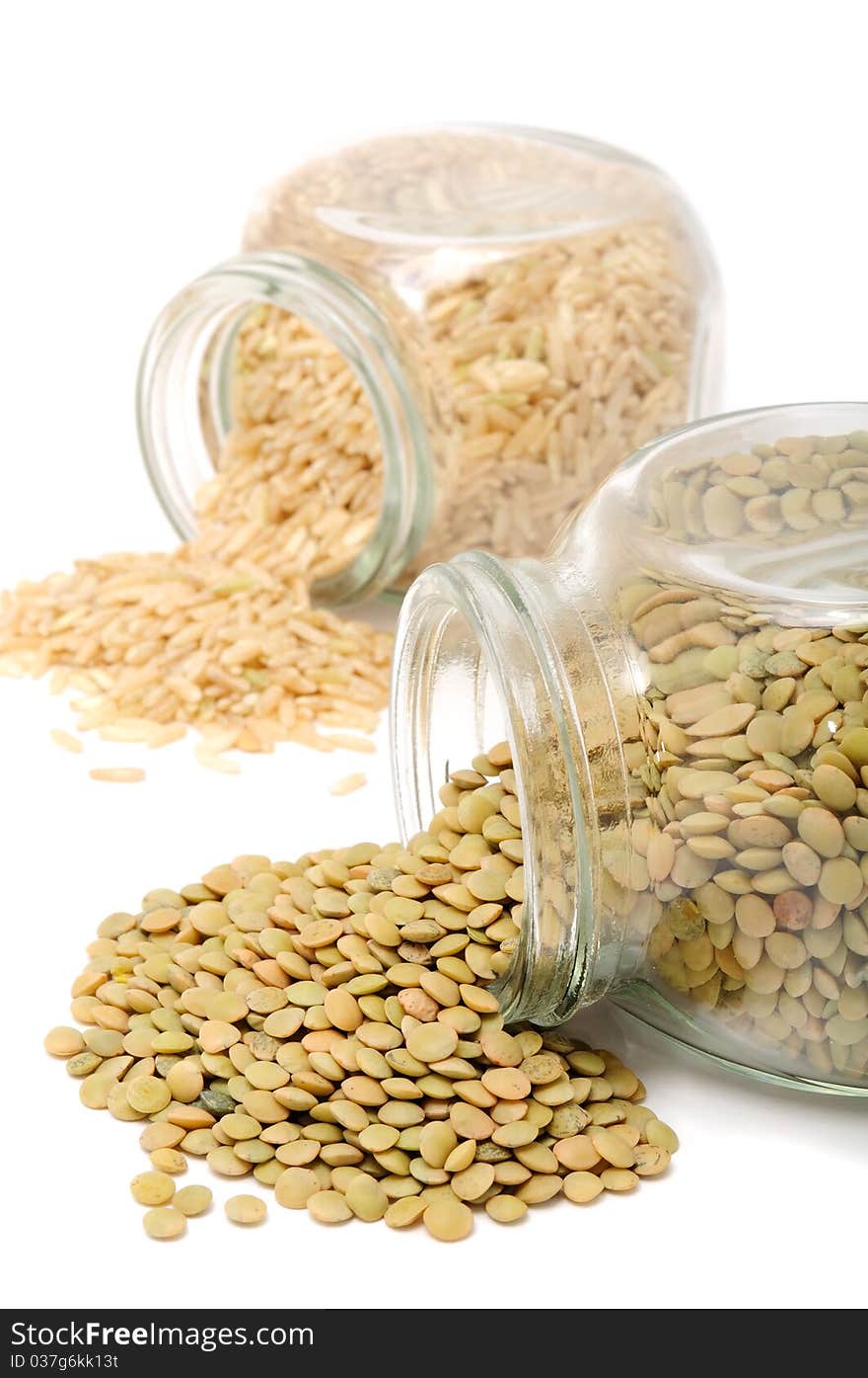 Glass jars with lentils and brown rice on a white background