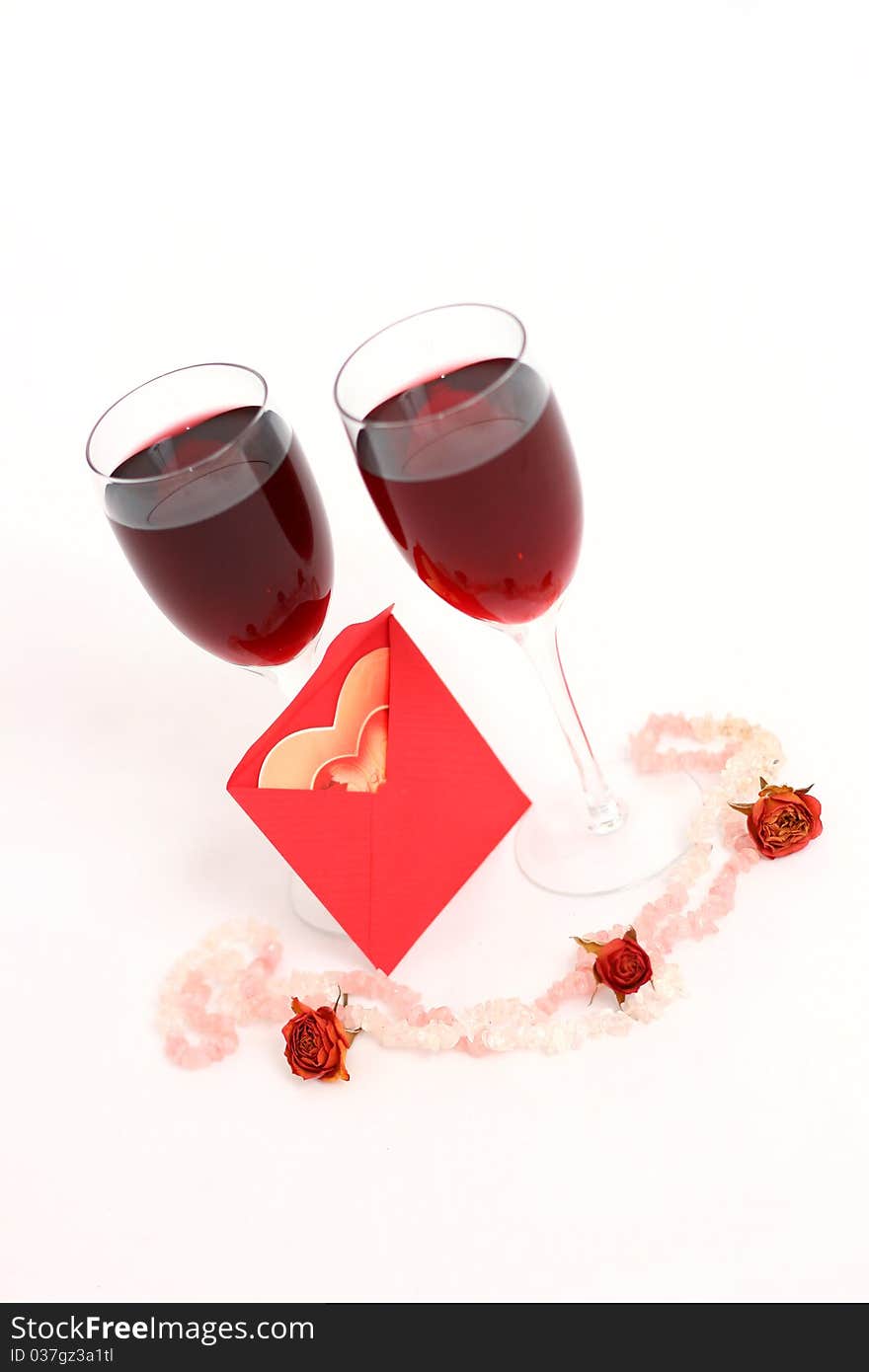 Two red wine glasses and a heart-shaped postcard in a red envelope. Two red wine glasses and a heart-shaped postcard in a red envelope