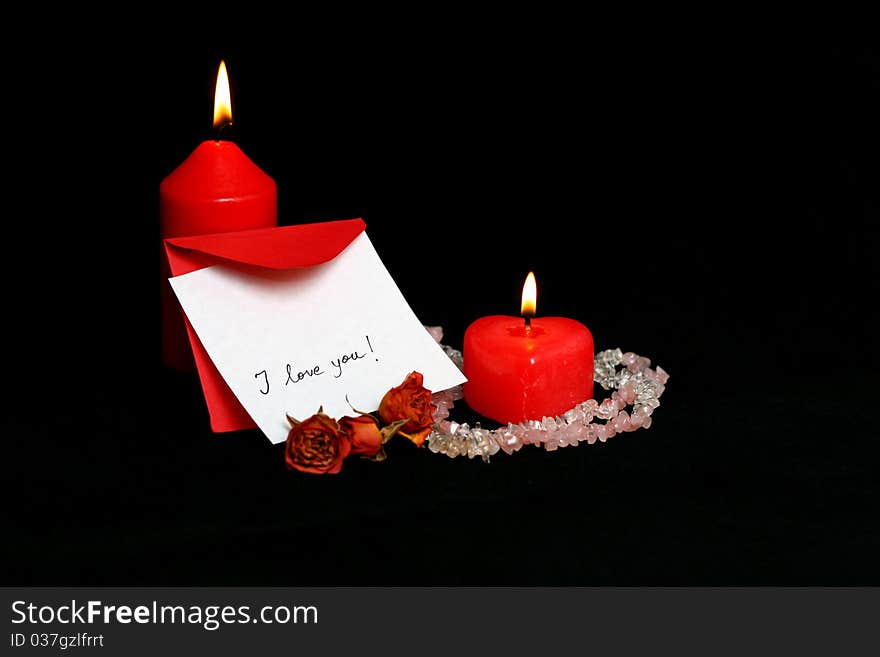 Love message handwritten on a white card with red envelope and burning red candles isolated on black. Love message handwritten on a white card with red envelope and burning red candles isolated on black