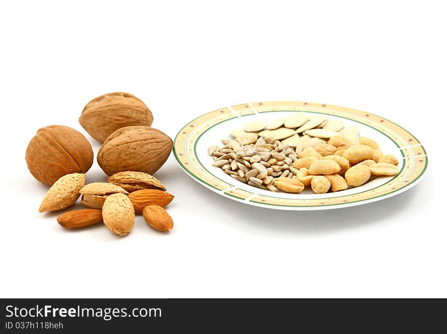 Mix of dry fruits (walnuts, almonds, peanuts) and a plate of seeds (sunflower and pumpkin seeds) isolated on white. Mix of dry fruits (walnuts, almonds, peanuts) and a plate of seeds (sunflower and pumpkin seeds) isolated on white