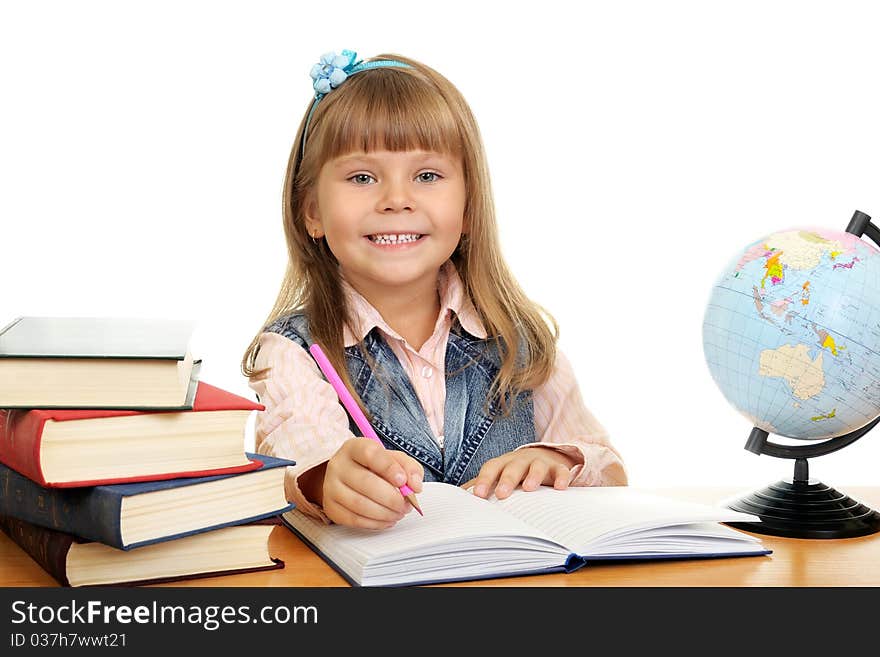 Smiling girl sits at a table and writes to writing-books. Globe on table. Photo Isolated over white. Smiling girl sits at a table and writes to writing-books. Globe on table. Photo Isolated over white