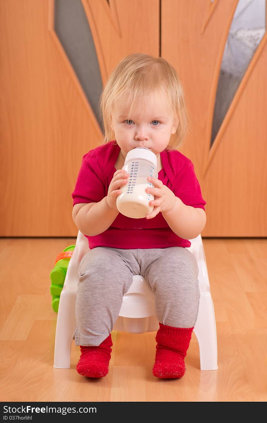 Adorable baby sit on baby chair toilet and drink milk from bottle