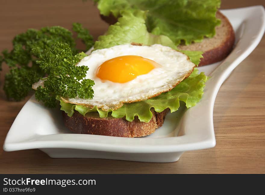 Sandwich with a fried egg on a white plate on a wooden surface. Sandwich with a fried egg on a white plate on a wooden surface