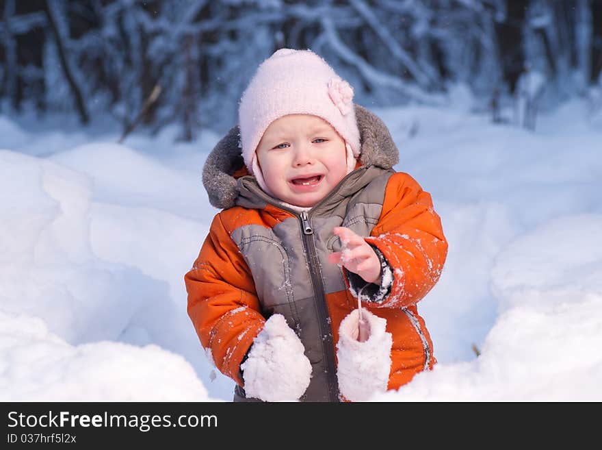 Adorable baby disappointed after eat cold snow in winter forest. Take away one mitten