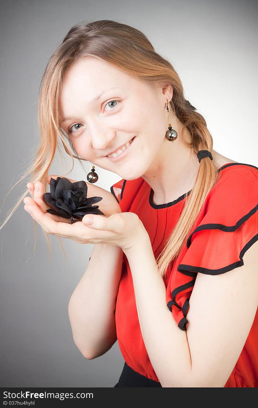 Beautiful blond woman wears red dress, smells black flower, with grey background