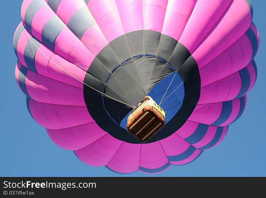 Low angle view of pink hot air balloon in flight with blue sky background.